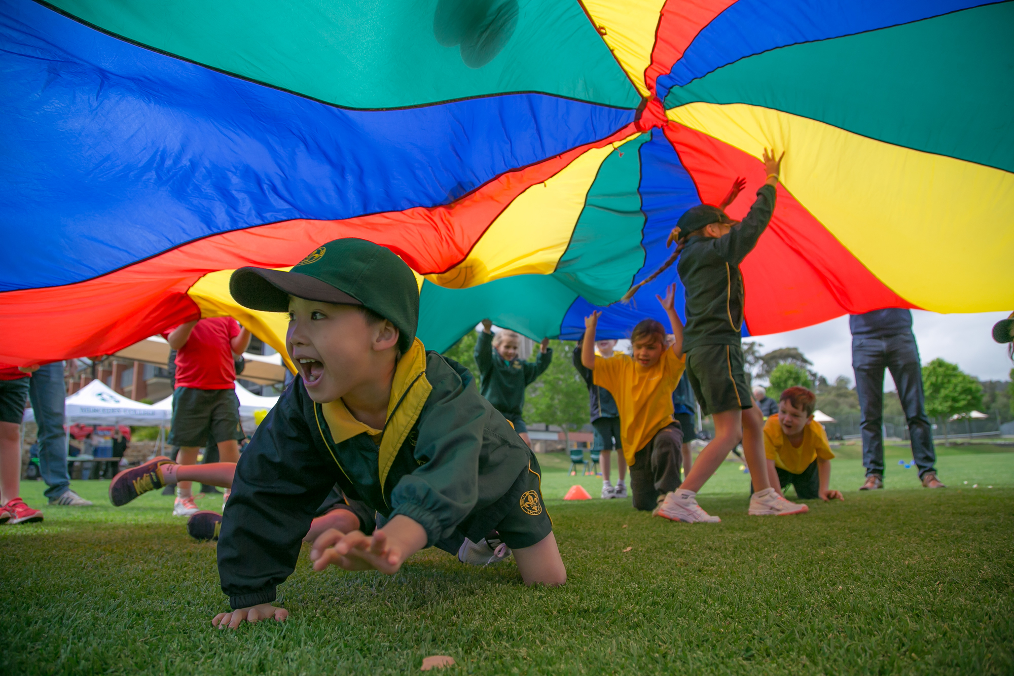 Young Mercedes College students playing under a colourful parachute on the oval.