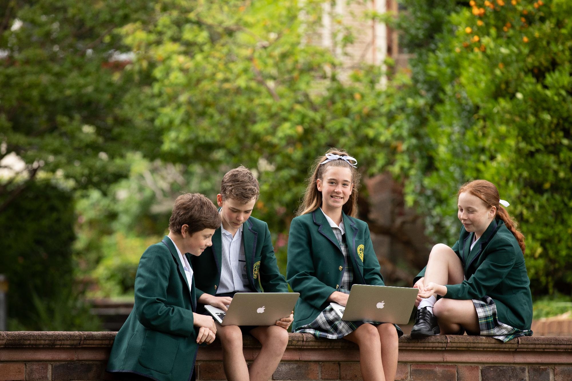 Group of students in Mercedes College uniforms learning outside with MacBooks.