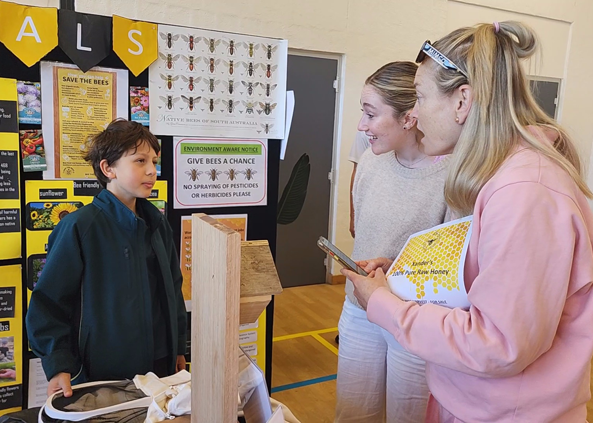 Mercedes College student presenting a bee conservation project to two visitors at school.