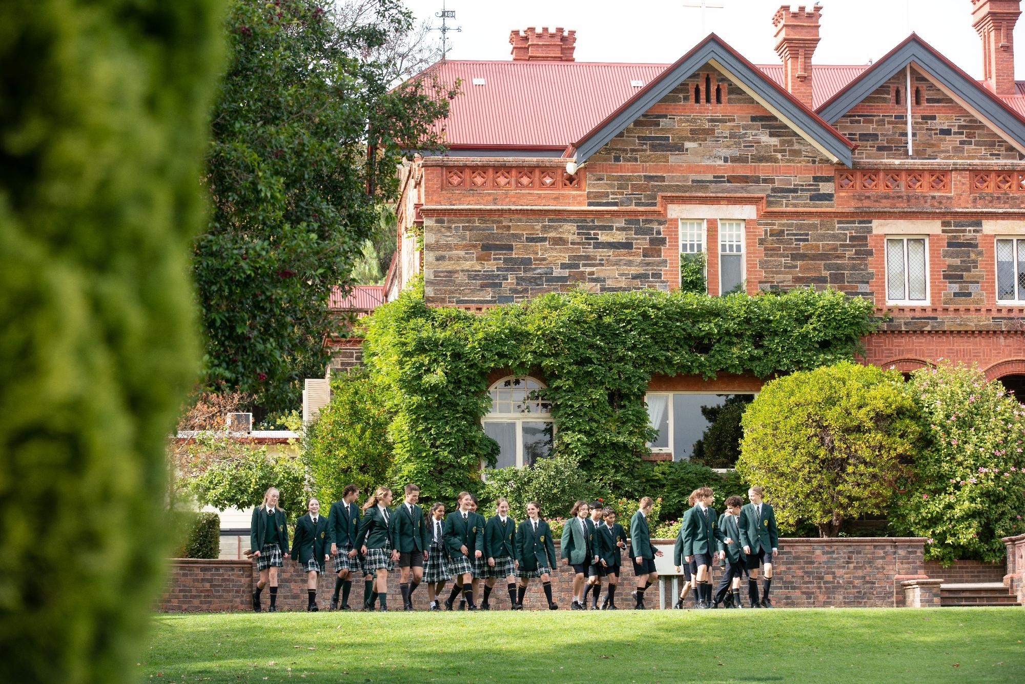 Mercedes College students walking in front of the historic heritage building surrounded by gardens.