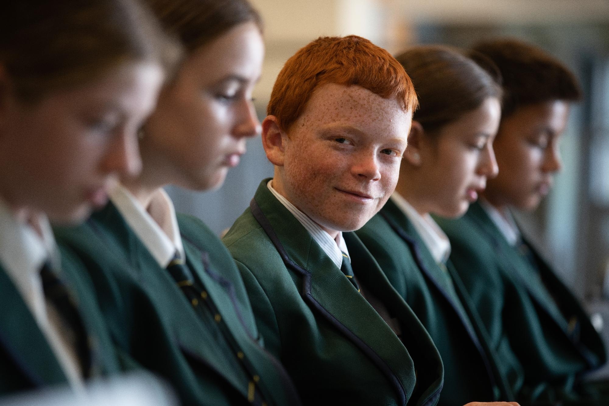 Group of Mercedes College students in green blazers, with a red-haired student looking towards the camera and smiling.