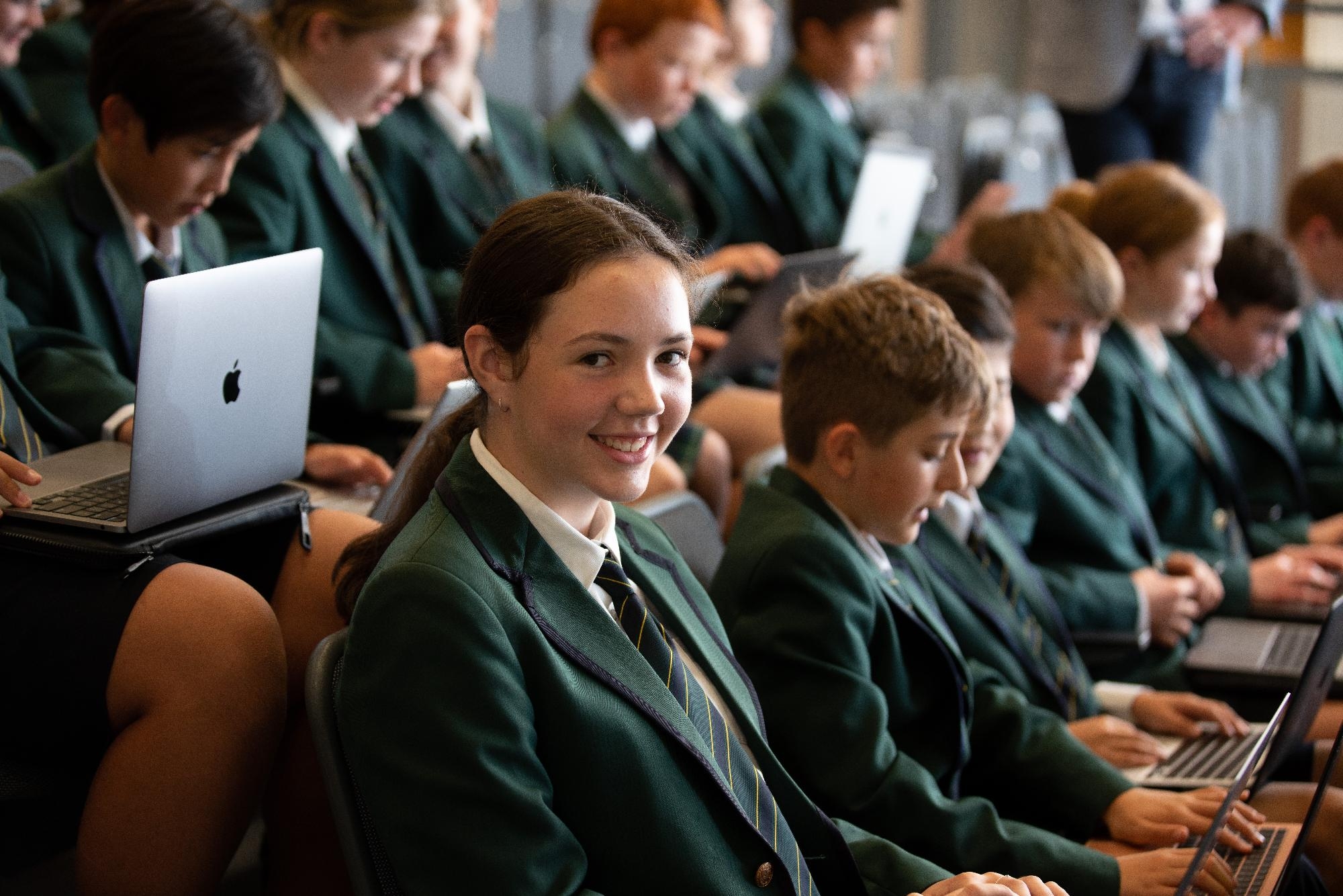 Mercedes College students focused on their studies with laptops, one girl smiling brightly.