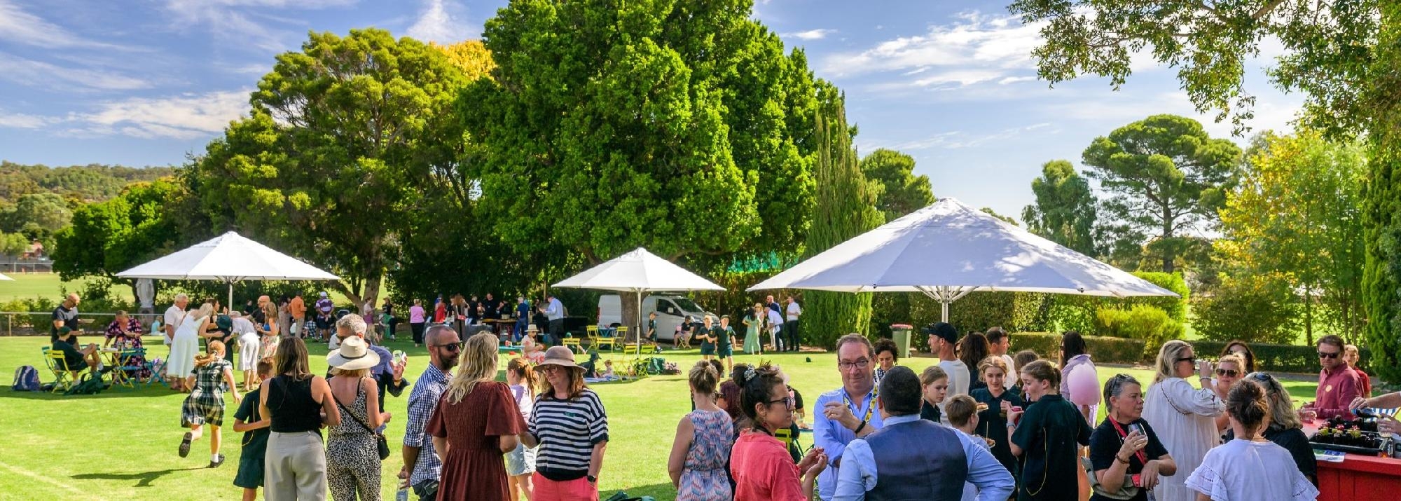 Parents, students, and staff mingling outdoors at a Mercedes College social gathering with food and drinks.