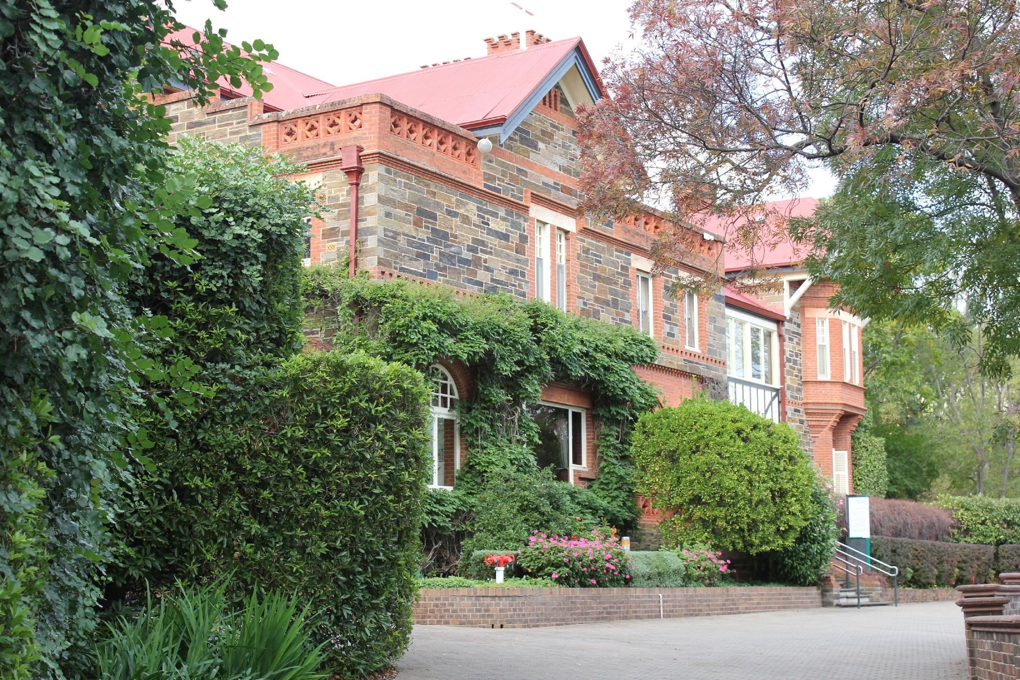 Heritage stone building with red roof surrounded by lush greenery at Mercedes College.