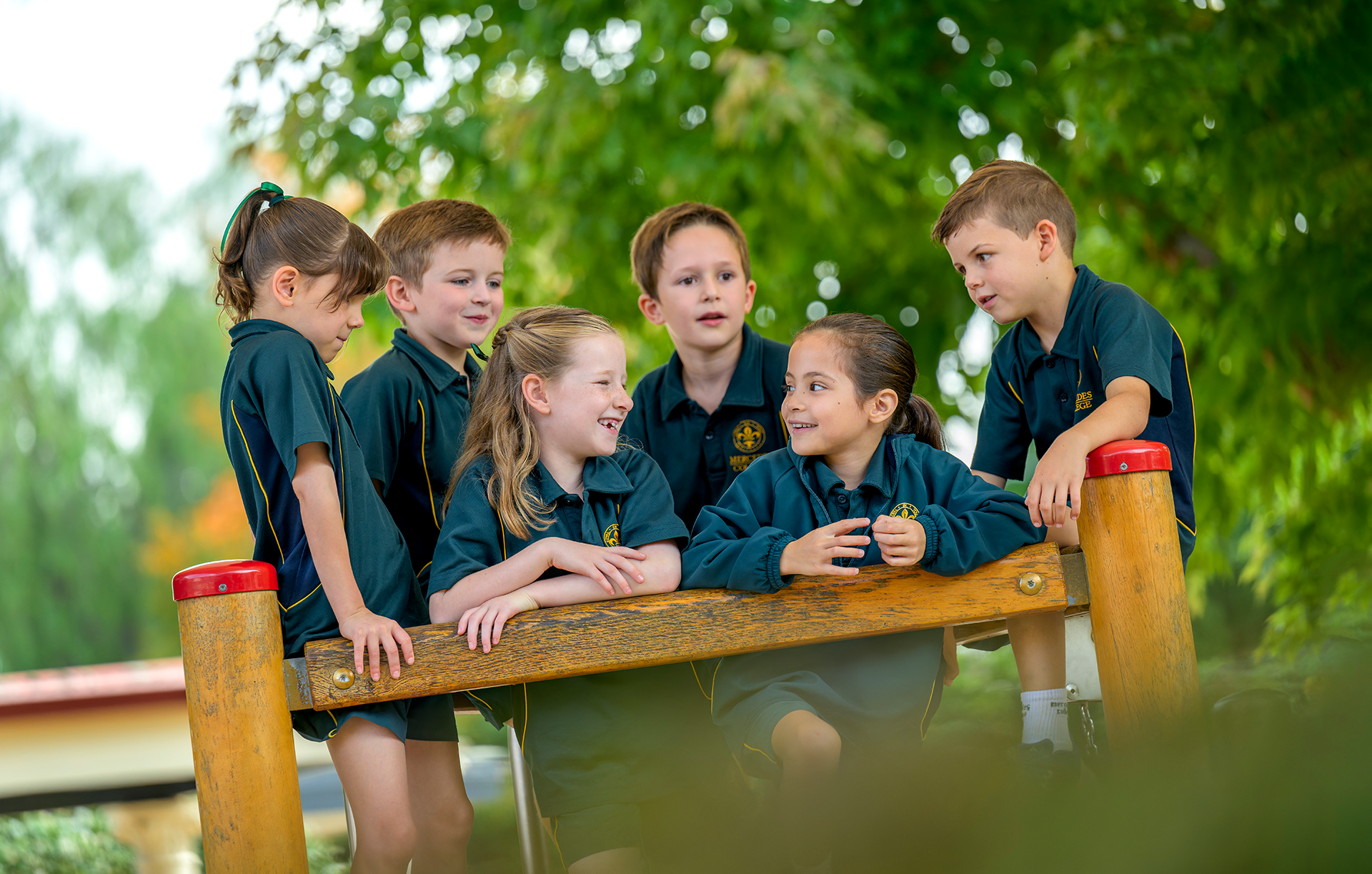 Mercedes College junior students sitting and talking together on outdoor playground equipment.