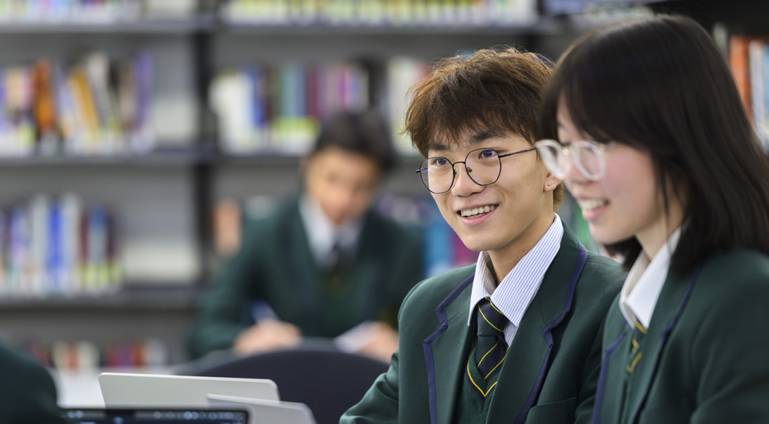 Smiling international students from Mercedes College engaging in classwork in the campus library setting.
