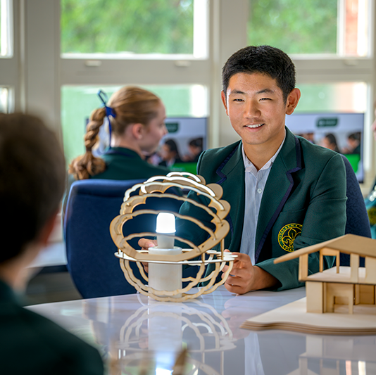 Mercedes College student presenting a modern wooden design prototype with a glowing light during a classroom project session.