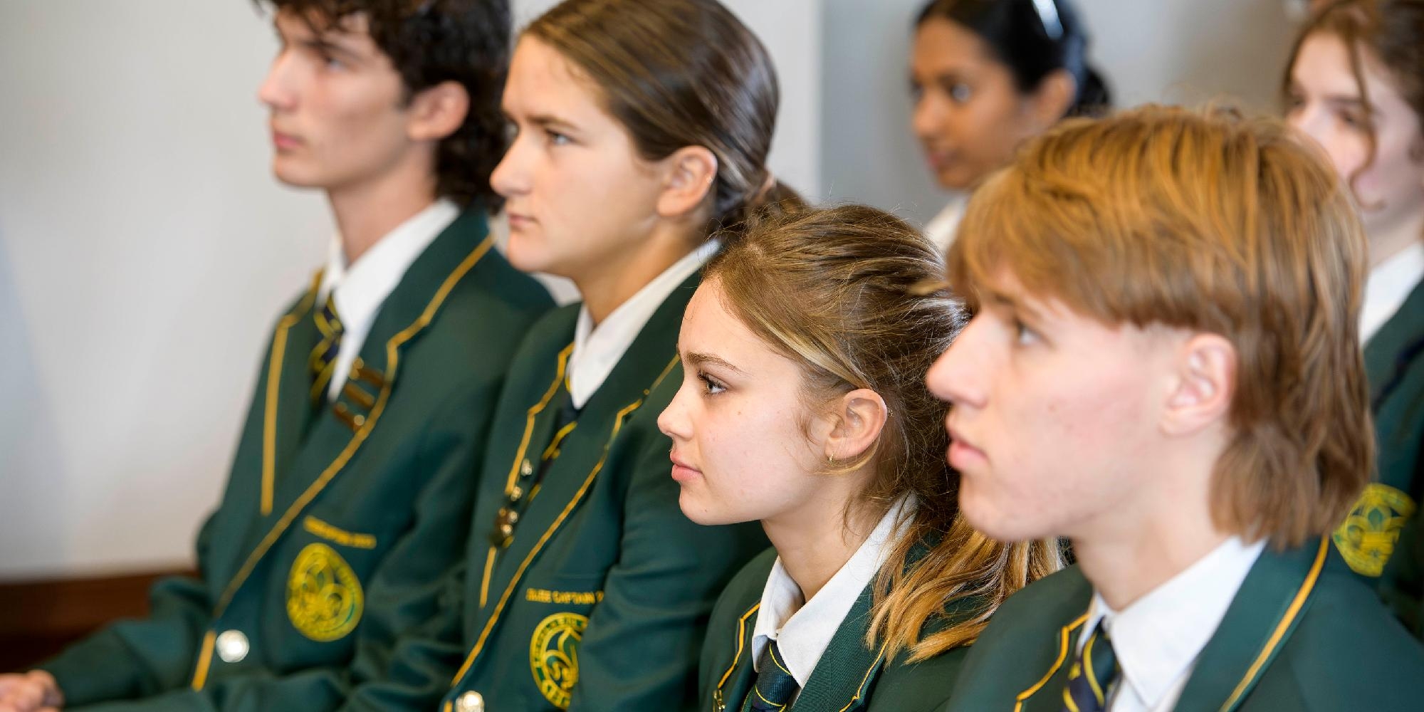 Focused Mercedes College students wearing formal blazers and ties during a presentation.