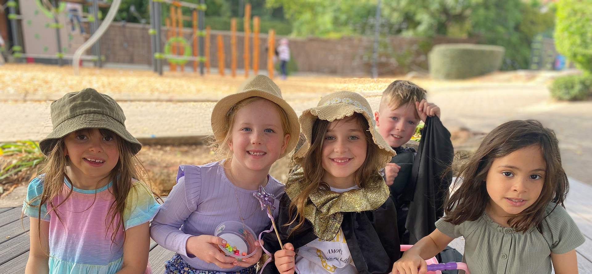 Group of Mercedes College junior students in hats and capes smiling together outdoors.