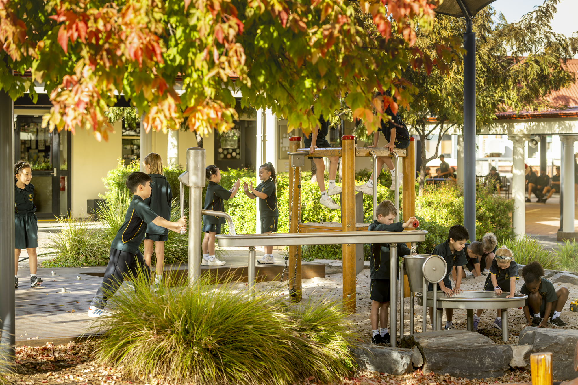 Young students in Mercedes College uniforms engaging in outdoor play at a nature-inspired playground surrounded by autumn leaves.